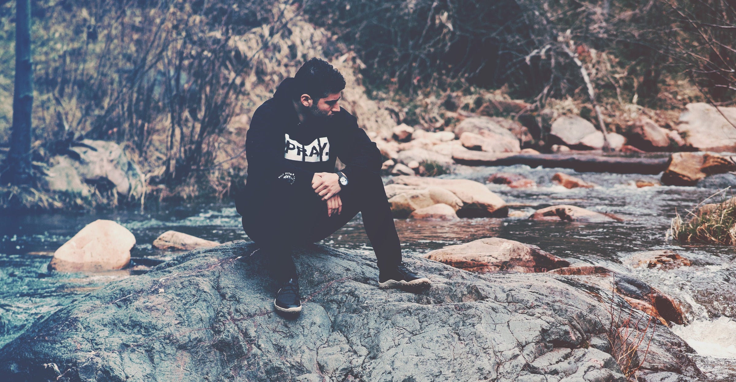 Zachary sitting on a rock by a stream in a forest